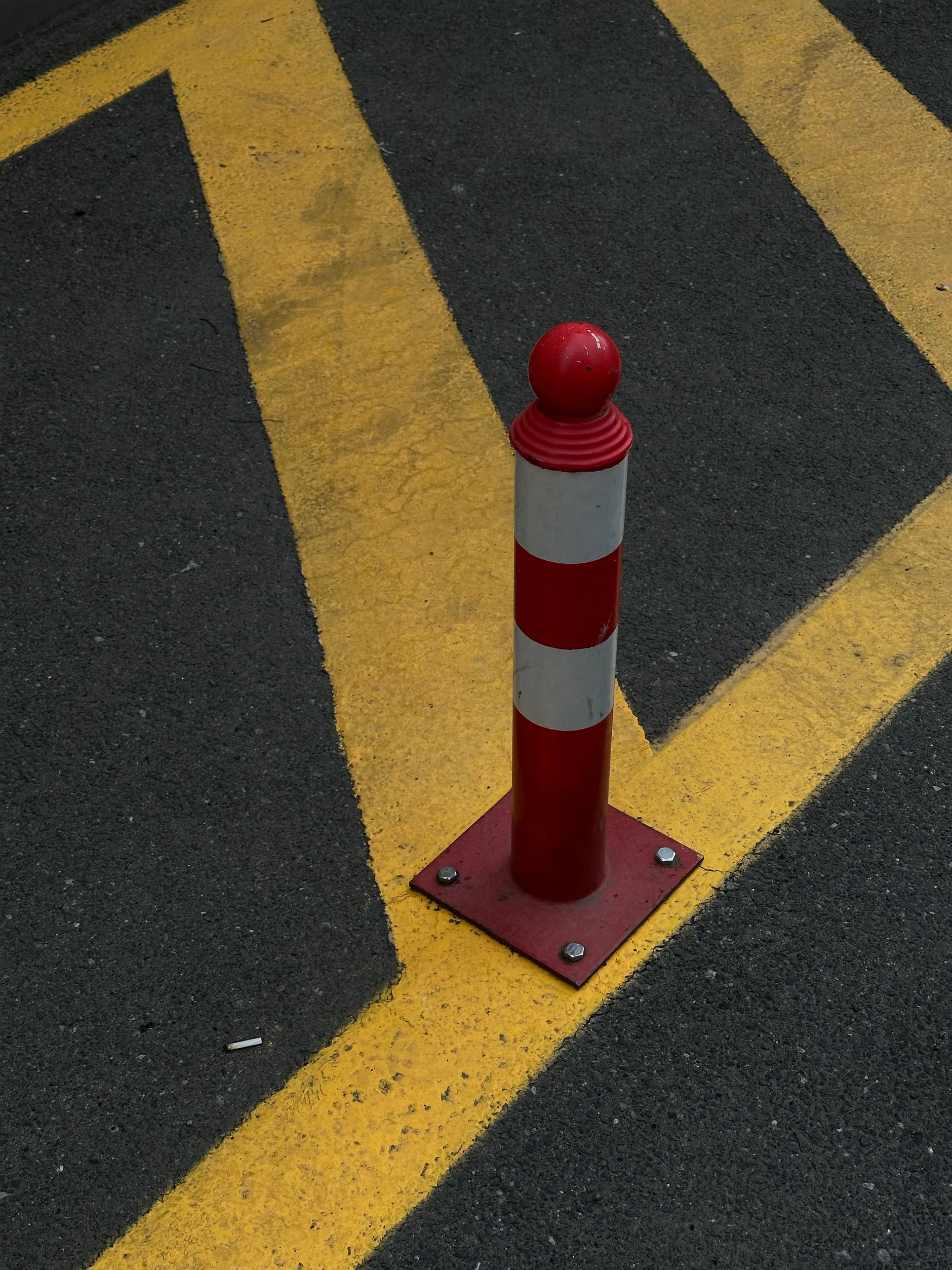 A red steel security bollard on an asphalt road, a physical vehicle barrier